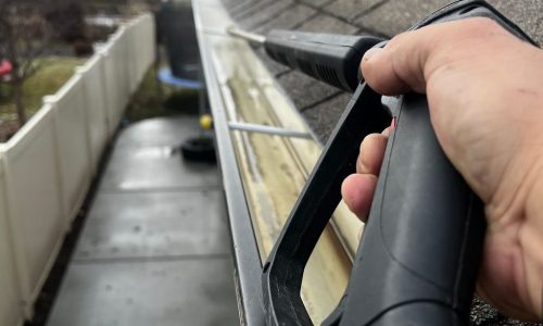 Close-up of gutter cleaning with pressure washer, outdoors, during the day.